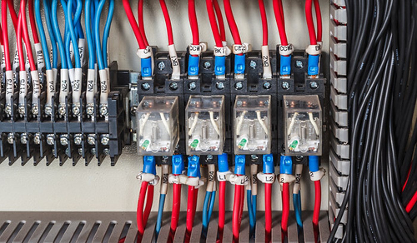 Gros plan sur l'intérieur d'une armoire électrique montrant quatre relais, des bornes et des fils bleus, rouges et noirs soigneusement câblés.