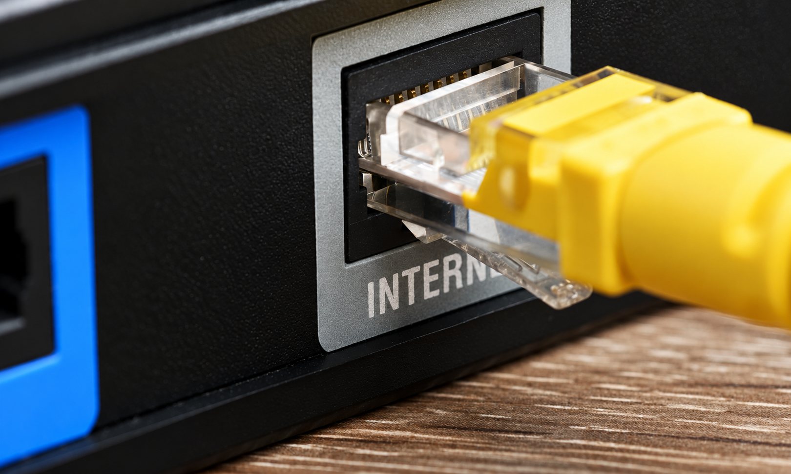 Gros plan d'un câble Ethernet jaune à embout transparent branché dans le port Internet à l'arrière d'un routeur noir posé sur une surface en bois.