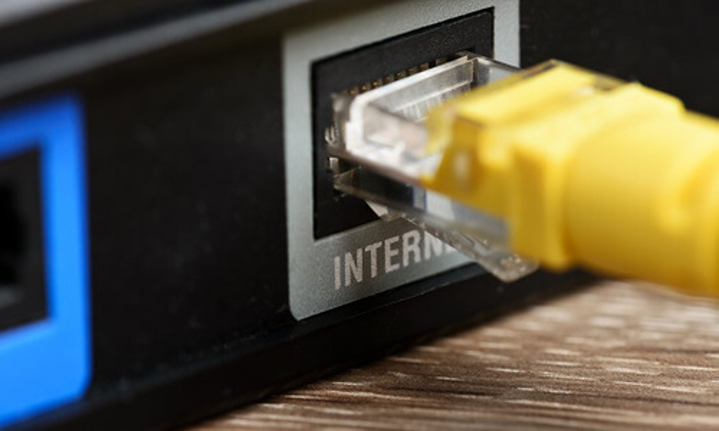 Gros plan sur un câble Ethernet jaune branché dans le port Internet à l'arrière d'un routeur noir posé sur une surface en bois.