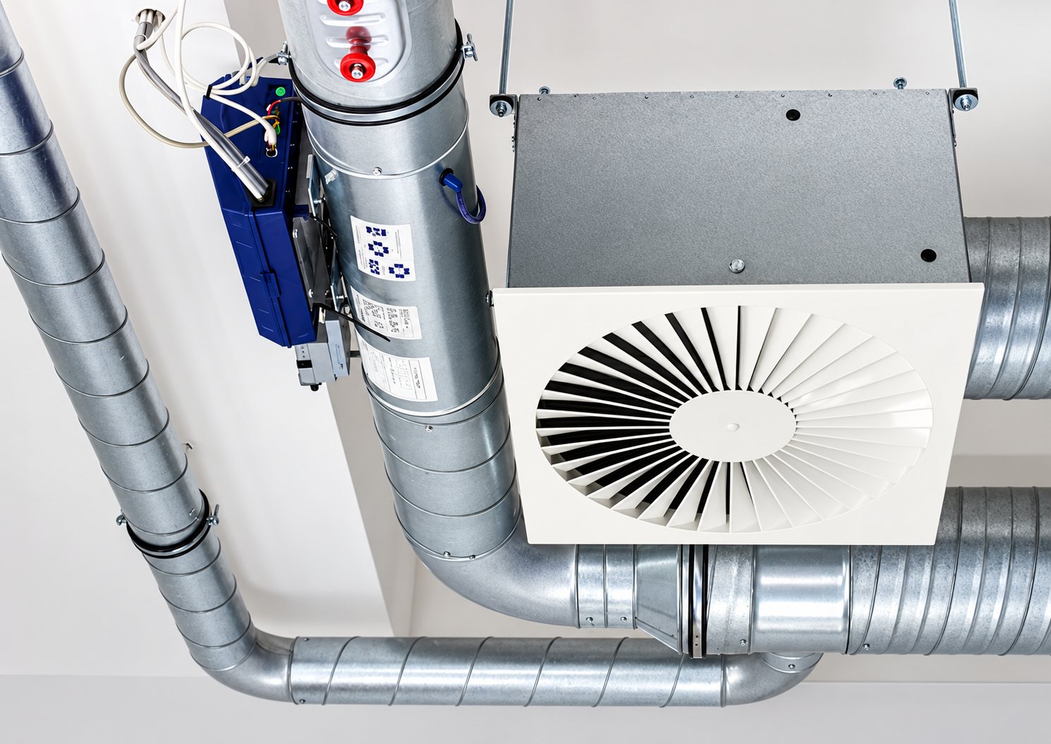 Installation de ventilation au plafond avec gaines métalliques galvanisées, un boîtier de régulation bleu et un diffuseur d'air blanc à ailettes circulaires.