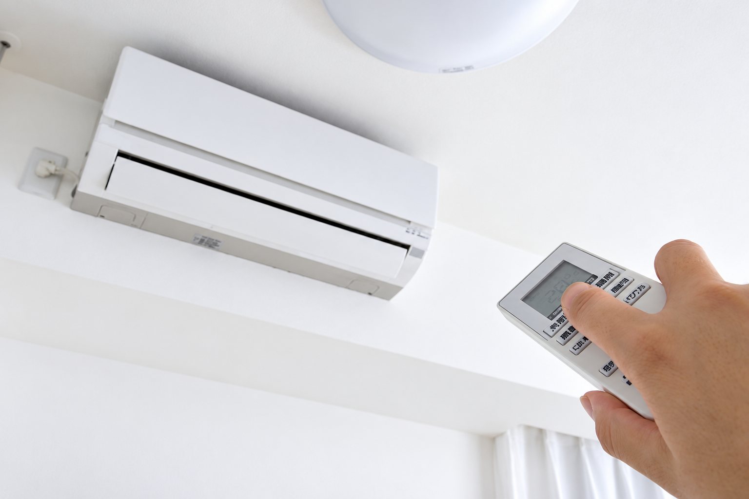 Une main tient une télécommande dirigée vers un climatiseur split mural blanc fixé sur un mur blanc.