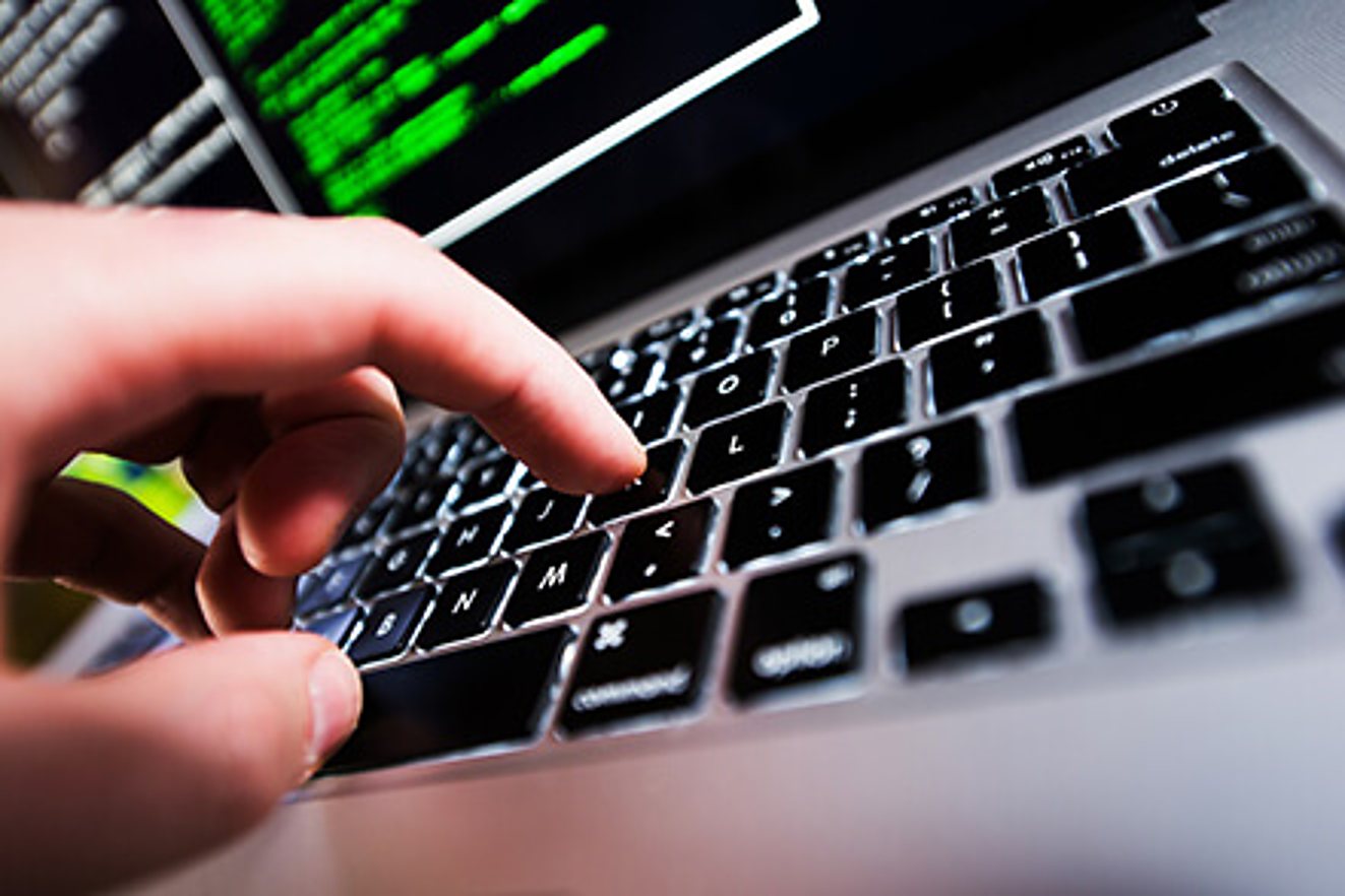 Gros plan d'une main qui appuie sur une touche du clavier d'un ordinateur portable dont l'écran affiche du texte vert sur fond noir.
